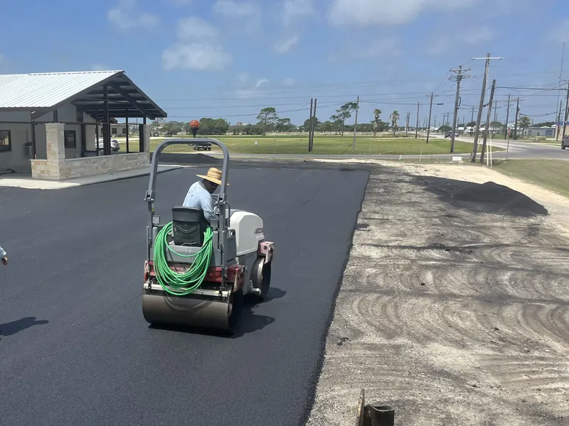 Roller compacting a fresh commercial lot beside a metal-roof business building