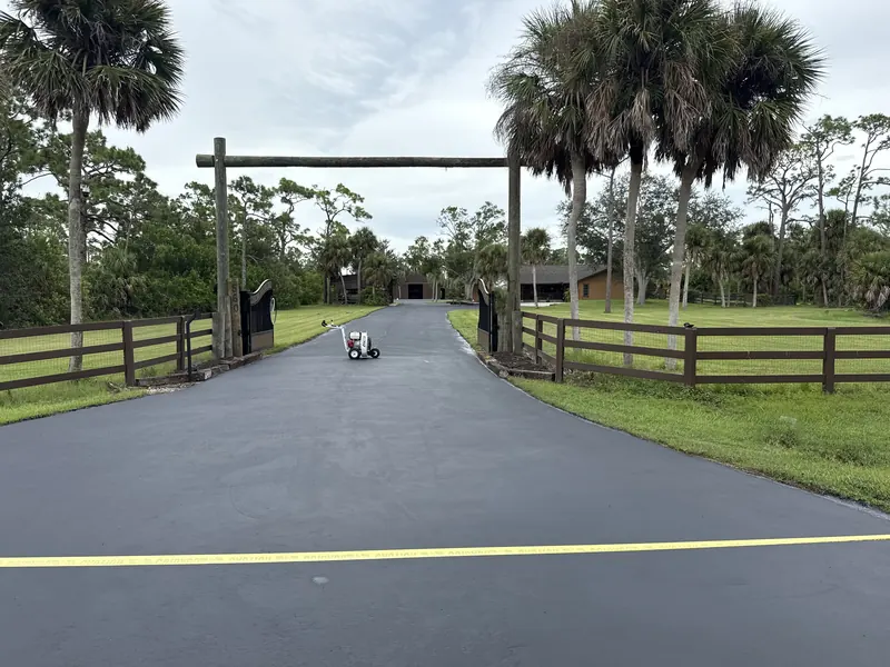 Freshly sealcoated driveway with a sealcoat sprayer, ranch gate and palms