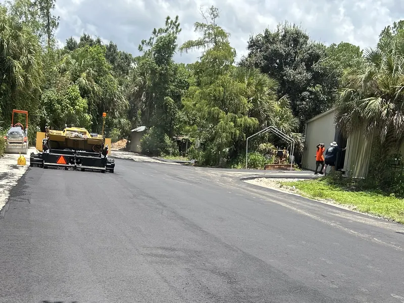 Asphalt paver laying a new road through palms and oaks